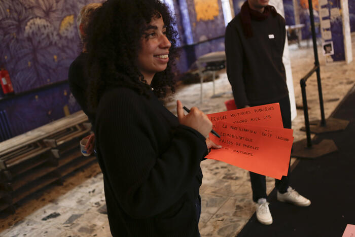 Rafaella Houlstan holding orange sheets of paper on which they are handwritten sentences in the pandora room in SeeU