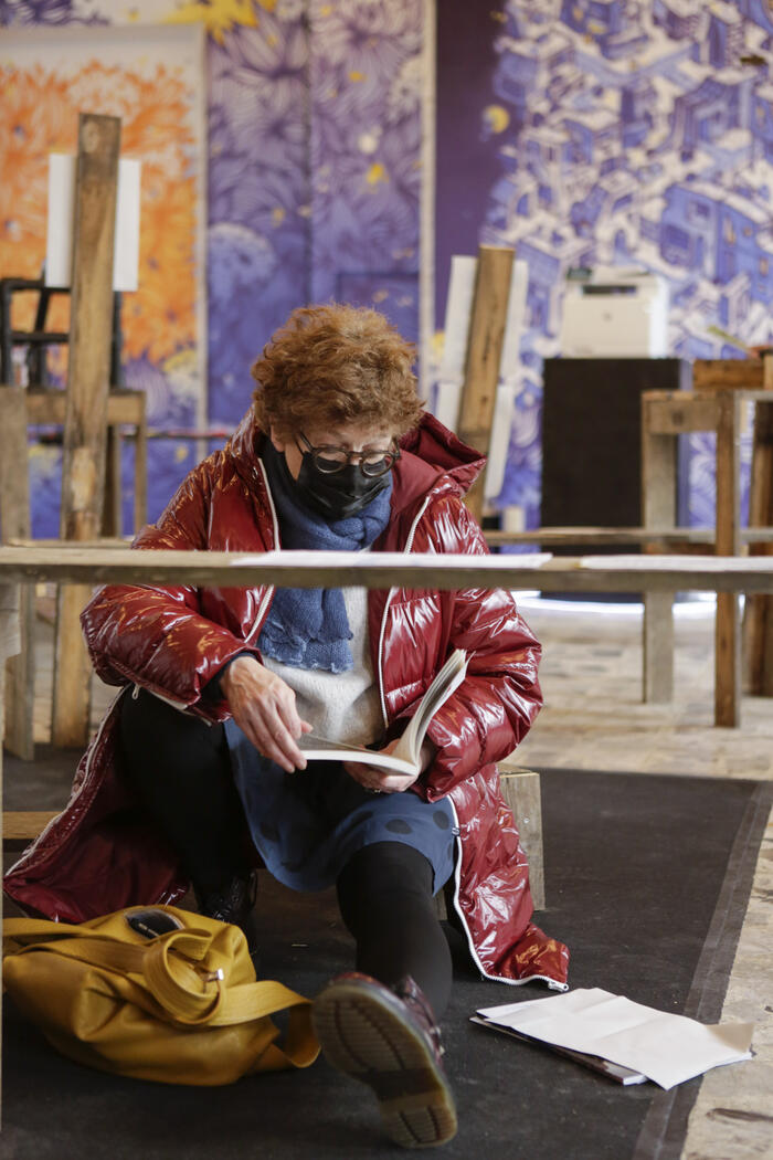 A person reading a piece of the exhibition seated on one of the exhibition furniture piece